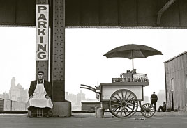 A food cart vender under a bridge waiting for customers.