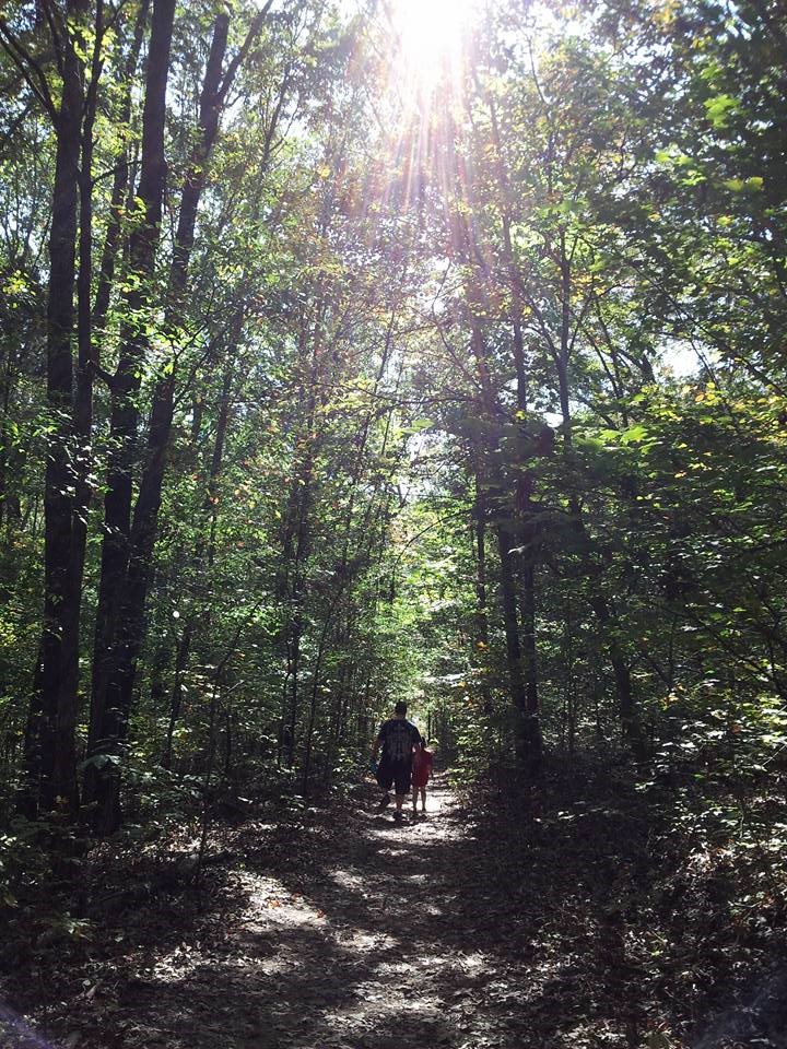 A child and father walks a trail in the woods at Dunbar Cave State Park.