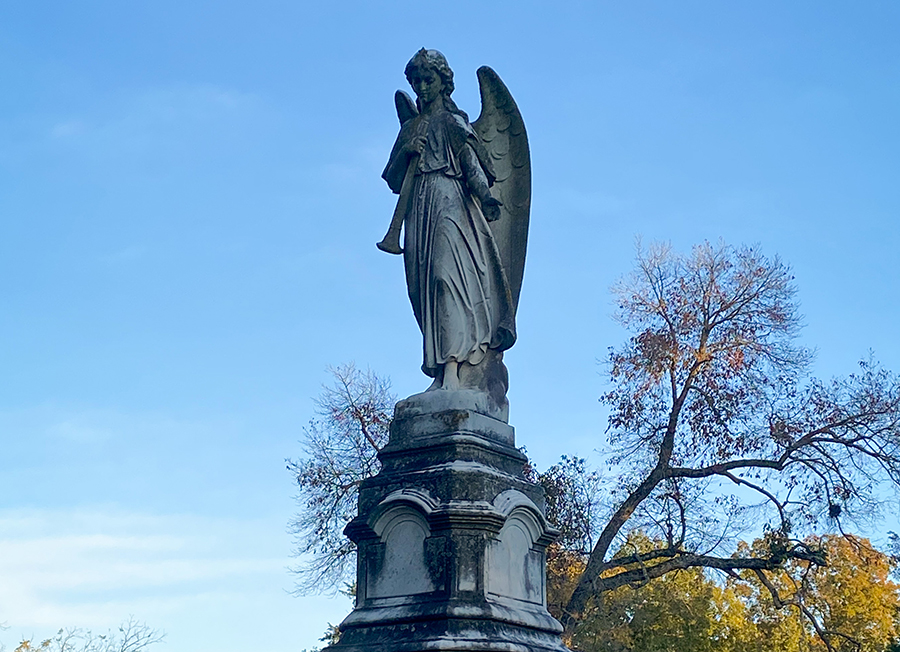 Ornate young, female angel holding a trumpet atop a marker at Greenwood Cemetery.