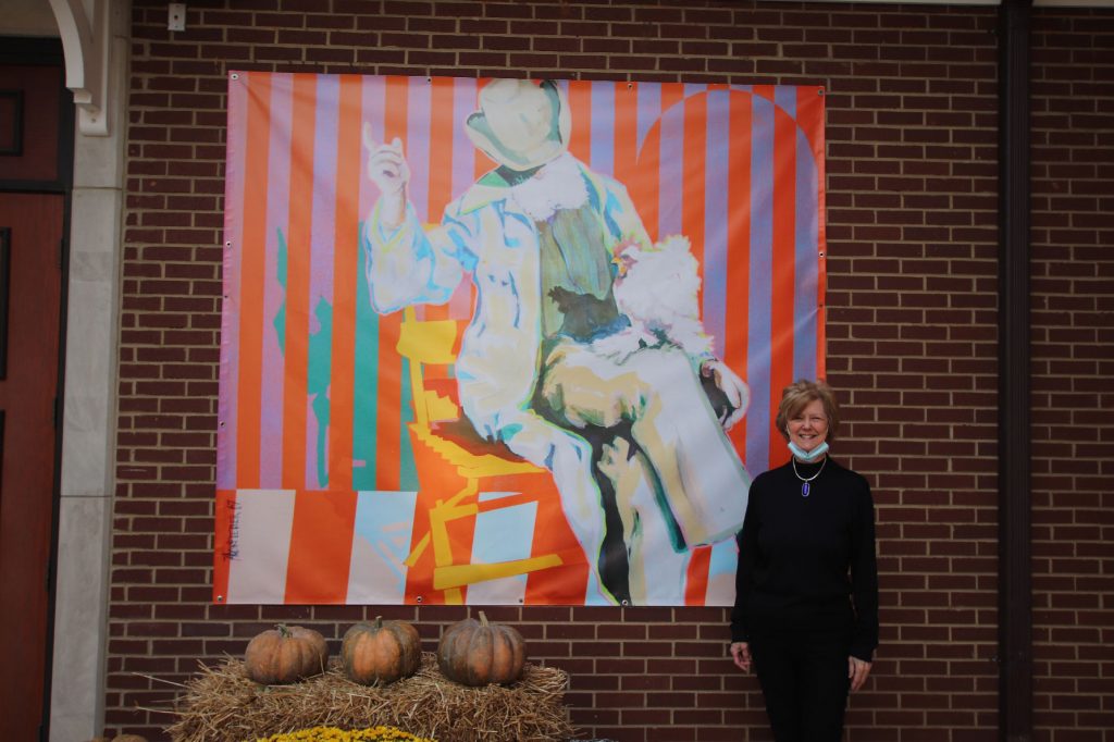Jacqueline Crouch stands in front of a new banner in the Museum courtyard of a painting she and her husband donated to the Museum.