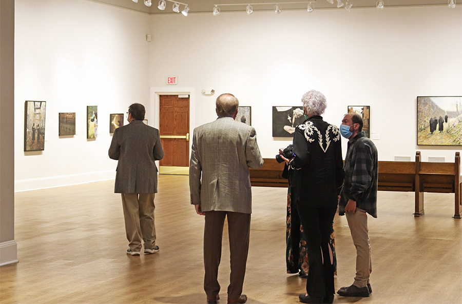 Museum visitors admire paintings hanging in a Museum gallery.