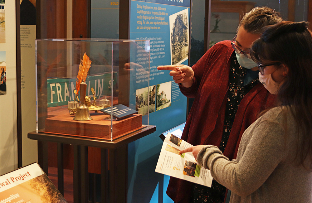 Mom and daughter check out quill pen artifact in the Becoming Clarksville exhibit. Mom points to artifact and daughter points to Museum Discovery Quest in her hands.