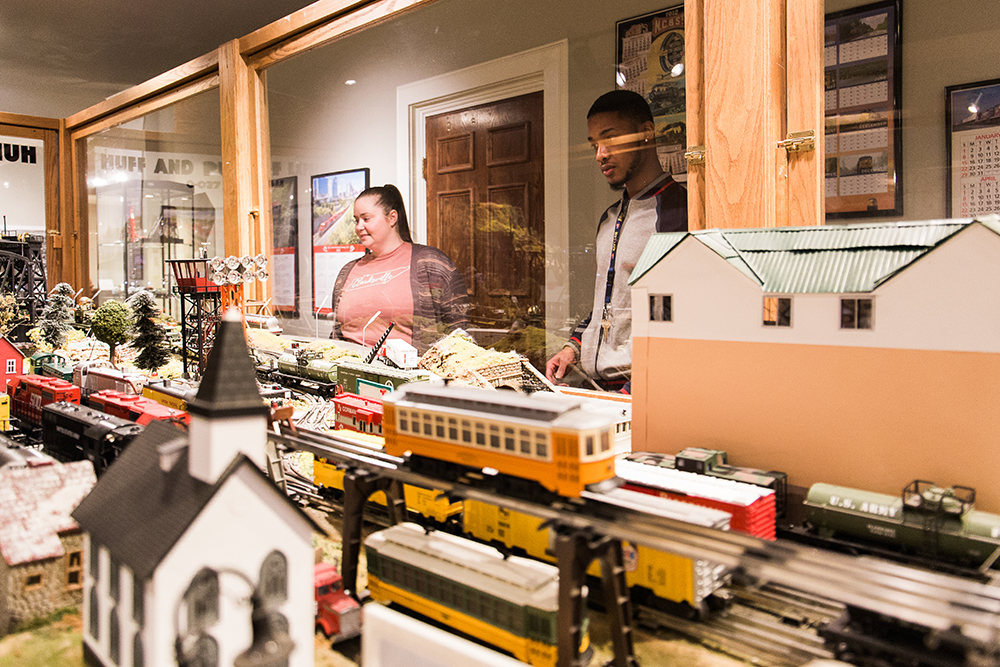 Two Museum guests watch the model trains glide by in the Huff & Puff Express Model Trains exhibit.