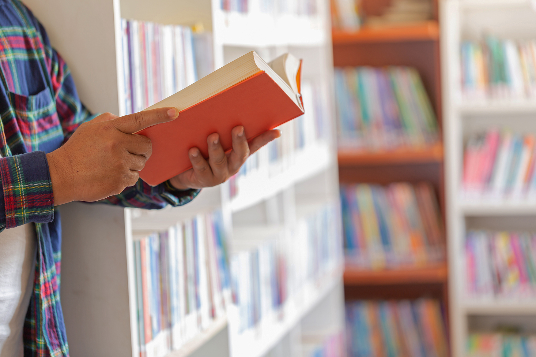 Image close-up of a person holding a book while standing around many bookshelves.