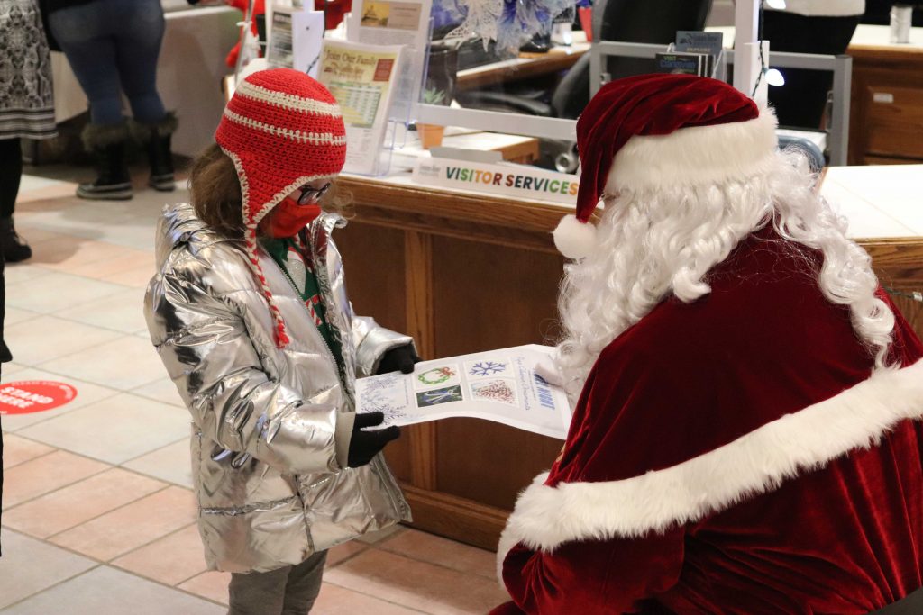 Santa hands a young girl a take-home activity packet at Noel Night