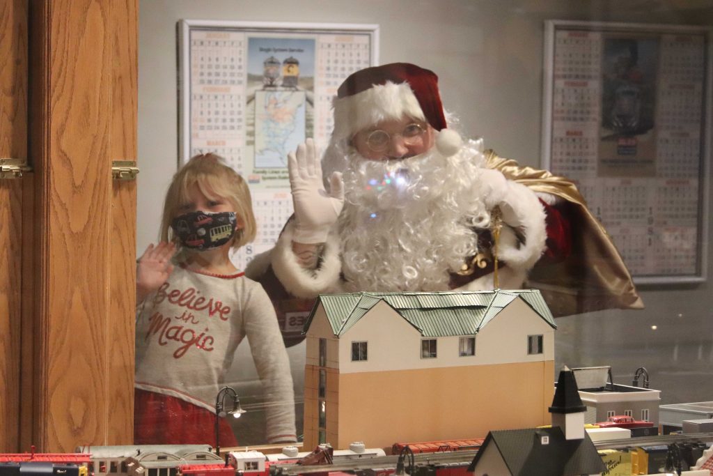 Santa and a young girl wave to the camera in the model train exhibit of the Museum